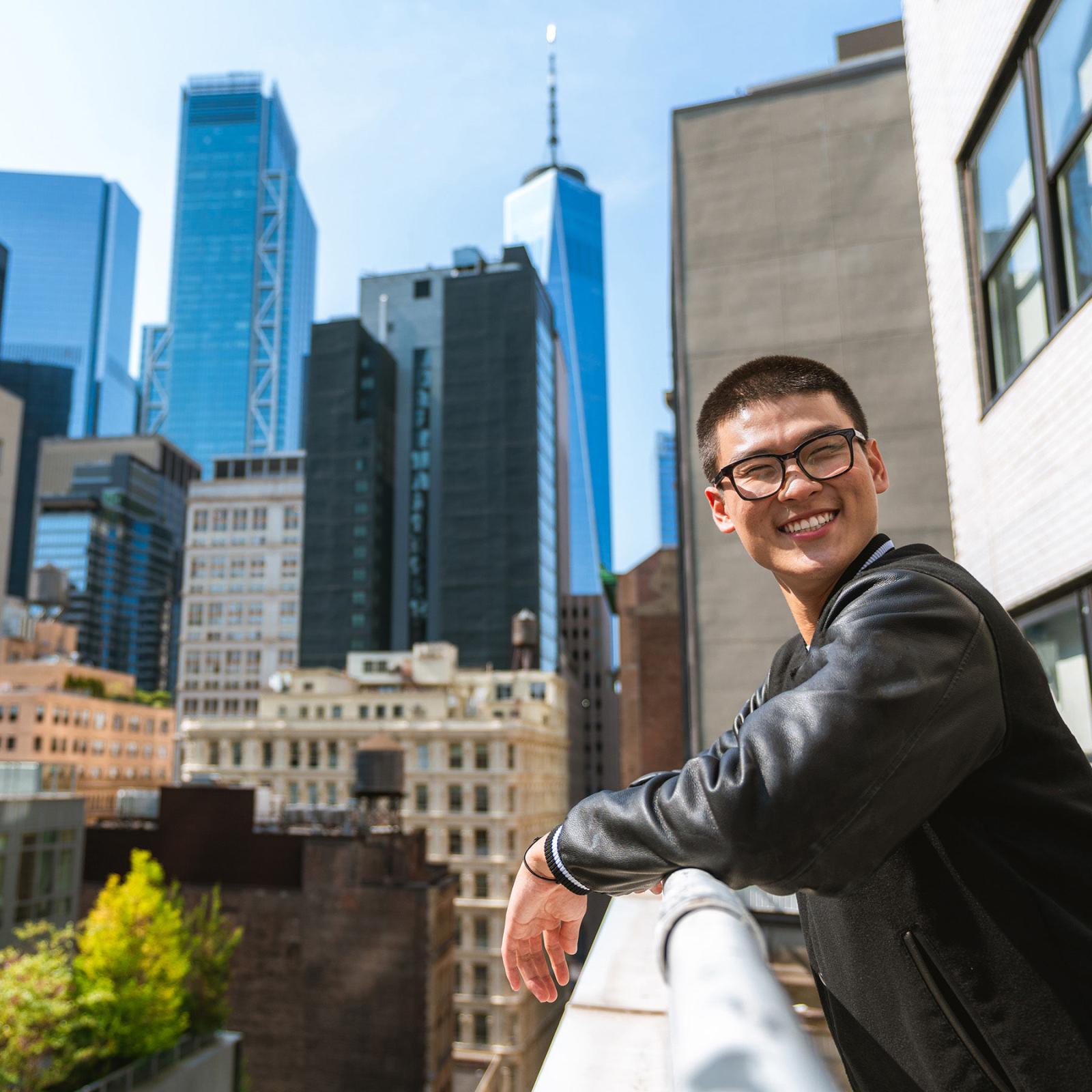 a ר student leans on a balcony with Manhattan buildings in the background